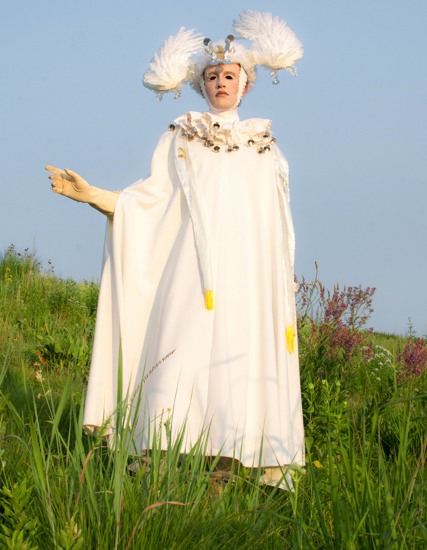 A figure in a white cloak with angel wing headpiece standing in a field